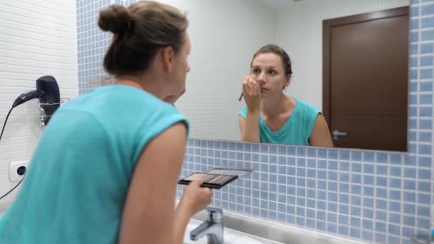 Bella donna fa trucco sopracciglio con ombretto e pennello trucco davanti allo specchio del bagno — Video Stock