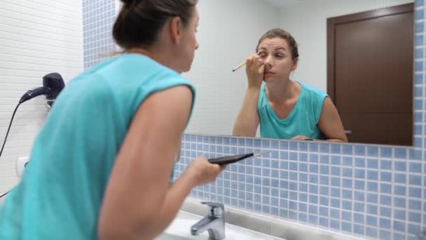 Mujer bonita haciendo maquillaje de ojos con sombra de ojos y cepillo de maquillaje delante del espejo del baño — Vídeos de Stock