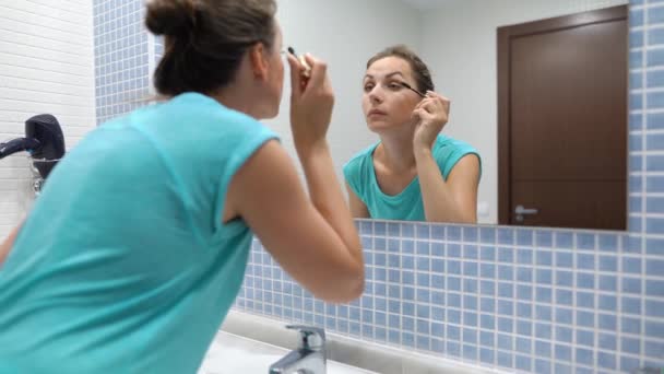 Mujer bonita aplicando rímel negro para el maquillaje de pestañas delante del espejo del baño — Vídeos de Stock