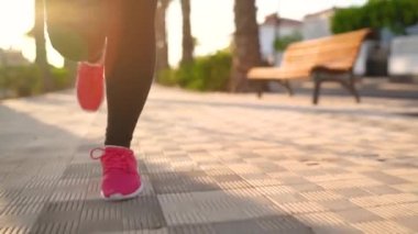 Gün batımında palmiye bulvarı boyunca koşan bir kadının bacaklarını kapatın. Yavaş çekim