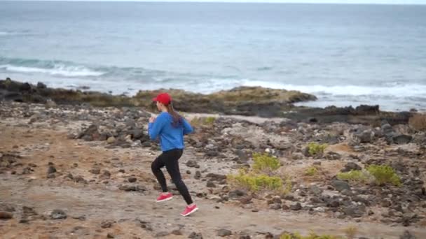 Жінка проходить уздовж кам'янистого берега океану. Здоровий активний спосіб життя. Повільний рух — стокове відео