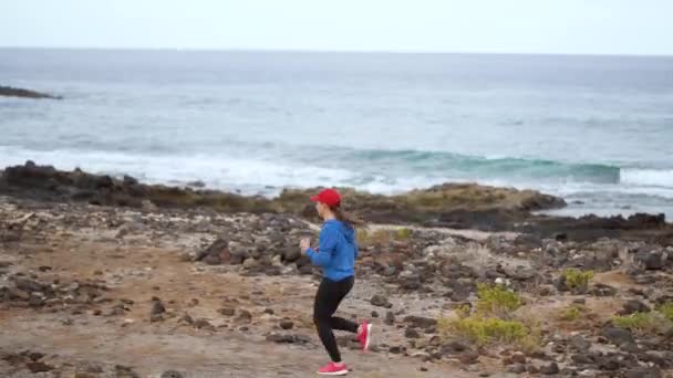 A mulher corre ao longo da costa pedregosa do oceano. Estilo de vida ativo saudável — Vídeo de Stock