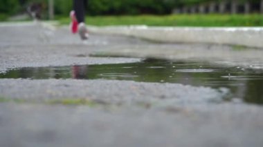 Spor ayakkabılı bir koşucunun bacakları. Spor kadını dışarıda koşuyor, çamurlu su birikintisine giriyor. Yağmurda koşan, su sıçratan tek koşucu. Yavaş çekim