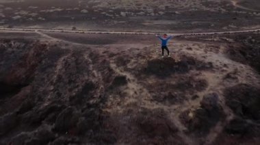 Spor giyimli kadın üzerinde uçmak, kolları yanlara kadar uzanmış bir kayanın üzerinde duruyor ve Atlantik Okyanusu'nun kıyısındaki bir koruma alanında manzaranın tadını çıkarıyor. Tenerife, Kanarya Adaları