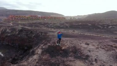 Koşu sonrası spor giyimli kadının havadan görünümü bir kayanın üzerinde duruyor ve Atlantik Okyanusu kıyılarındaki bir koruma alanında manzaranın keyfini çıkarıyor. Tenerife, Kanarya Adaları, İspanya