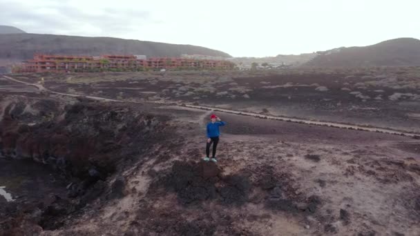 Vista aérea de la mujer en ropa deportiva después de correr se encuentra en la parte superior de una roca y disfruta del paisaje en un área de conservación a orillas del Océano Atlántico. Tenerife, Islas Canarias, España — Vídeos de Stock