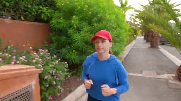 Frau joggt entlang der Straße inmitten der tropischen Allee — Stockvideo