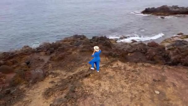 Güzel mavi elbise ve şapka lı bir kadının havadan görünümü, Atlantik Okyanusu kıyılarındaki bir koruma alanında bir dağın tepesinde duruyor. Tenerife, Kanarya Adaları, İspanya — Stok video
