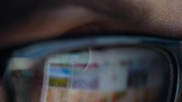 Woman in glasses looking on the monitor and surfing Internet. The monitor screen is reflected in the glasses — Stock Video