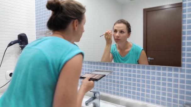 La mujer hace una rutina matutina: se cepilla los dientes, maquilla y se pone el pelo . — Vídeos de Stock