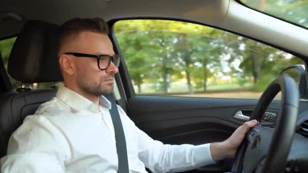 Hombre barbudo en gafas y camisa blanca conduciendo un coche en tiempo soleado. Vista lateral — Vídeos de Stock