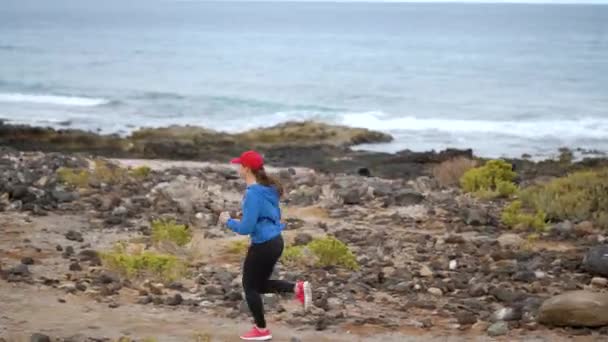 A mulher corre ao longo da costa pedregosa do oceano. Estilo de vida ativo saudável — Vídeo de Stock