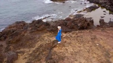 Güzel mavi elbise ve şapka lı bir kadının havadan görünümü, Atlantik Okyanusu kıyılarındaki bir koruma alanında bir dağın tepesinde duruyor. Tenerife, Kanarya Adaları, İspanya