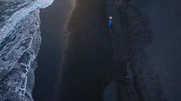 Gün batımında siyah kum ile sahilde yürüyen mavi elbiseli bir kızın üst görünümü. Tenerife, Kanarya Adaları, İspanya — Stok video