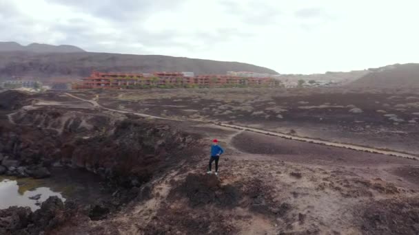 Vista aérea de la mujer en ropa deportiva después de correr se encuentra en la parte superior de una roca y disfruta del paisaje en un área de conservación a orillas del Océano Atlántico. Tenerife, Islas Canarias, España — Vídeos de Stock