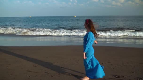 Kobieta w pięknej niebieskiej sukni i okulary oferuje spacer wzdłuż plaży, z radością przędzenia. Zwolnionym — Wideo stockowe