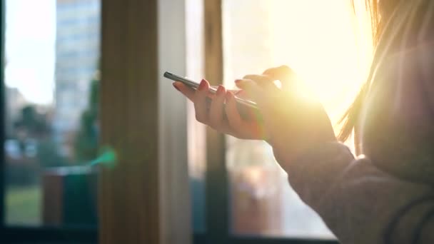 Mãos femininas usando smartphone contra uma paisagem urbana turva no pôr do sol — Vídeo de Stock