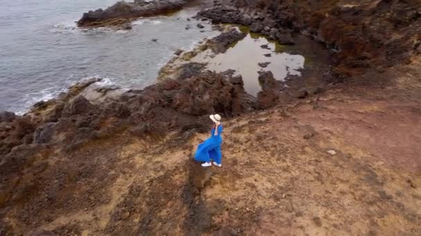 Aerial syn på kvinnan i en vacker blå klänning och hatt står på toppen av ett berg i ett naturskyddsområde vid stranden av Atlanten. Teneriffa, Kanarieöarna, Spanien — Stockvideo