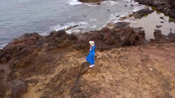 Aerial syn på kvinnan i en vacker blå klänning och hatt står på toppen av ett berg i ett naturskyddsområde vid stranden av Atlanten. Teneriffa, Kanarieöarna, Spanien — Stockvideo