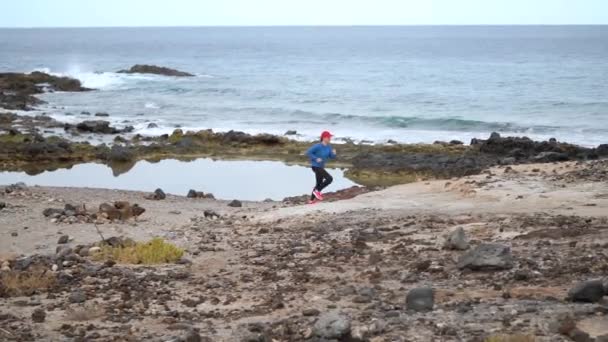 Una donna corre lungo la riva pietrosa dell'oceano. Stile di vita sano e attivo. Rallentatore — Video Stock