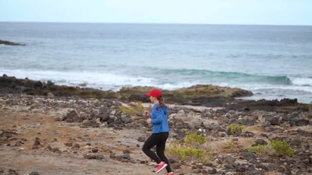 A mulher corre ao longo da costa pedregosa do oceano. Estilo de vida ativo saudável. Movimento lento — Vídeo de Stock