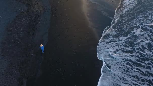 Повітряна думка дівчини в синьому вбранні, що ходить на пляжі з чорним піском на заході сонця. Тенеріфе, Канарські острови, Іспанія — стокове відео