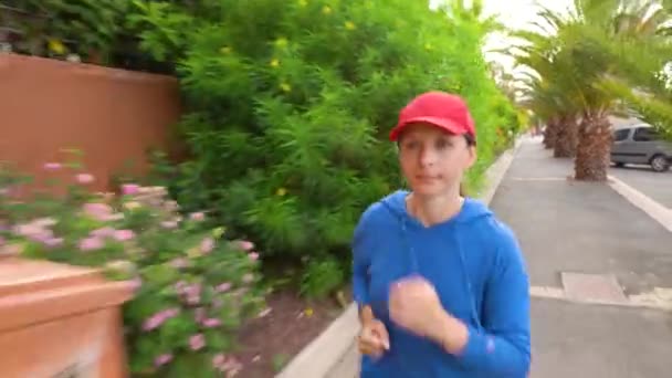 Жінка біжить по вулиці серед тропічної алеї — стокове відео