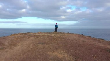 Spor giyimli bir kadının üzerinde uçmak bir kayanın üzerinde durur ve Atlantik Okyanusu kıyısındaki bir koruma alanında manzaranın tadını çıkarır. Tenerife, Kanarya Adaları