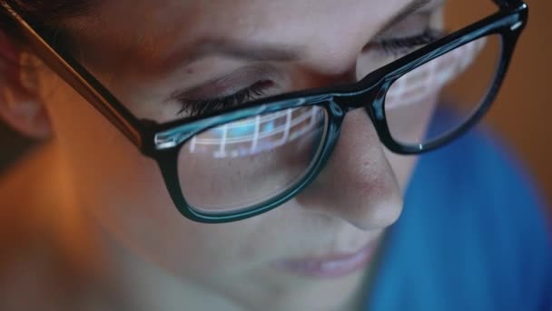 Woman in glasses looking on the monitor and surfing Internet. The monitor screen is reflected in the glasses — Stock Video
