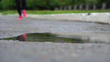 Spor ayakkabılı bir koşucunun bacakları. Spor kadını dışarıda koşuyor, çamurlu su birikintisine giriyor. Tek koşucu yağmurda çalışan, sıçrama yapma.