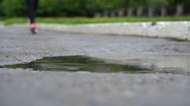 Spor ayakkabılı bir koşucunun bacakları. Spor kadını dışarıda koşuyor, çamurlu su birikintisine giriyor. Tek koşucu yağmurda çalışan, sıçrama yapma