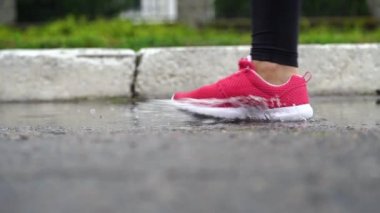 Spor ayakkabılı bir koşucunun bacakları. Spor kadını dışarıda koşuyor, çamurlu su birikintisine giriyor. Yağmurda koşan, su sıçratan tek koşucu. Yavaş çekim