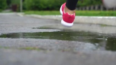 Spor ayakkabılı bir koşucunun bacakları. Spor kadını dışarıda koşuyor, çamurlu su birikintisine giriyor. Tek koşucu yağmurda çalışan, sıçrama yapma