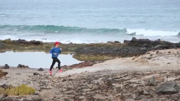 La mujer corre a lo largo de la costa pedregosa del océano. Vida activa saludable — Vídeo de stock