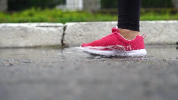 Jambes d'un coureur en baskets. Femme sportive faisant du jogging à l'extérieur, se jetant dans la flaque boueuse. Un seul coureur court sous la pluie, faisant des éclaboussures. Mouvement lent 