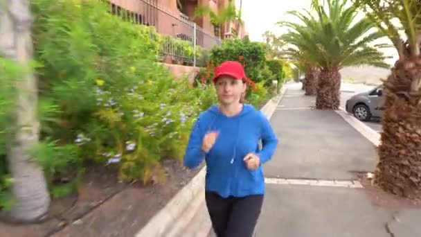 Vrouw joggen langs de straat tussen de tropische steeg — Stockvideo