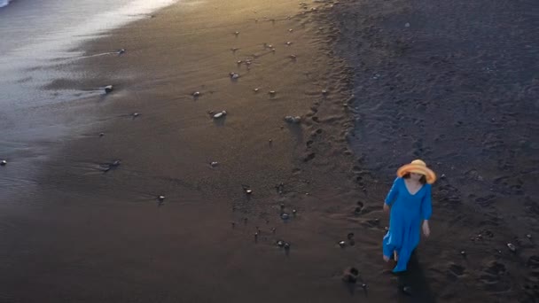 Luftaufnahme eines Mädchens in einem blauen Kleid, das bei Sonnenuntergang am Strand mit schwarzem Sand spaziert. Teneriffa, Kanarische Inseln, Spanien — Stockvideo