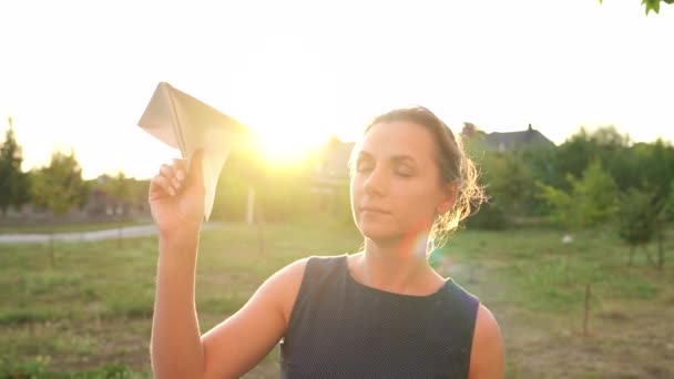Η γυναίκα εγκαινιάζει χαρτί αεροπλάνο κατά ηλιοβασίλεμα φόντο. Ονειρευόσασταν να ταξιδέψετε ή το επάγγελμα μιας αεροσυνοδών — Αρχείο Βίντεο