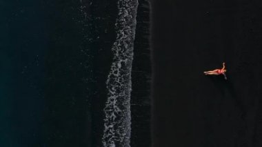 Sörf çizgisinde siyah bir plajda uzanan kırmızı mayo giymiş bir kızın en iyi görüntüsü. Tenerife adasının kıyıları, Kanarya Adaları, İspanya.