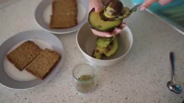 Avokado tostu pişirme süreleri: Kadın avokadoyu keser, posasını çıkarır, doğrar ve üzerine ekmek, tuz ve baharat serper.
