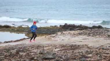Kadın okyanusun taşlı kıyısında koşuyor. Sağlıklı aktif yaşam tarzı. Yavaş hareket