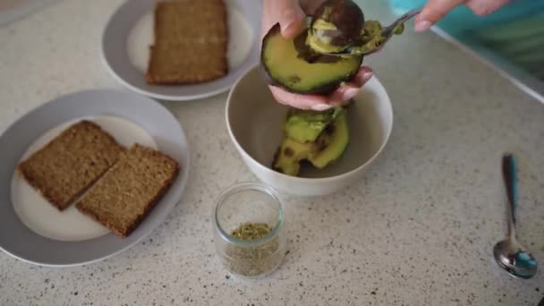 Zeitraffer beim Kochen von Avocado-Toast - Frau schneidet die Avocado und nimmt das Fruchtfleisch heraus, hackt es und legt Brot, Salz und Gewürze darüber. — Stockvideo