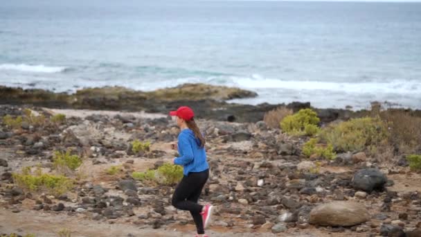 Kobieta biegnie wzdłuż kamiennego brzegu oceanu. Zdrowy, aktywny tryb życia. Zwolnionym — Wideo stockowe