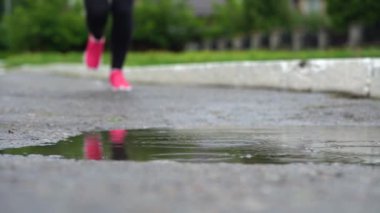 Spor ayakkabılı bir koşucunun bacakları. Spor kadını dışarıda koşuyor, çamurlu su birikintisine giriyor. Tek koşucu yağmurda çalışan, sıçrama yapma.