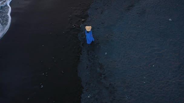 Luftaufnahme eines Mädchens in einem blauen Kleid, das am Strand mit schwarzem Sand spaziert. Teneriffa, Kanarische Inseln, Spanien — Stockvideo