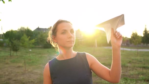 女性は日没の背景に紙飛行機を起動します。旅行やスチュワーデスの職業の夢。スローモーション — ストック動画