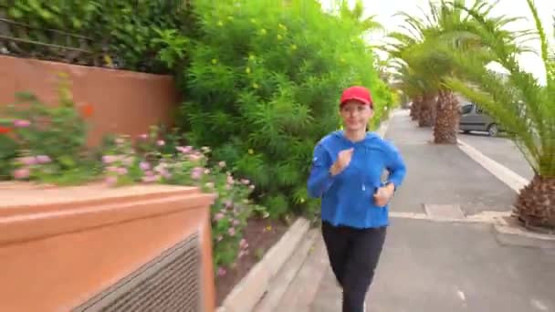 Vrouw joggen langs de straat tussen de tropische steeg — Stockvideo
