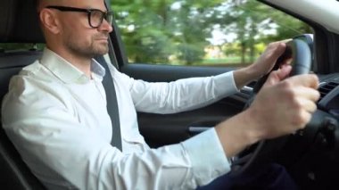 Güneşli havalarda araba kullanan gözlüklü ve beyaz gömlekli sakallı adam. Yan görünüm