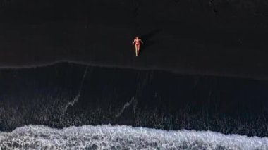 Sörf çizgisinde siyah bir plajda uzanan kırmızı mayo giymiş bir kadının en iyi görüntüsü. Tenerife adasının kıyıları, Kanarya Adaları, İspanya.