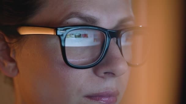 Mulher de óculos olhando no monitor e navegando na Internet. A tela do monitor é refletida nos óculos — Vídeo de Stock